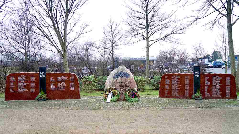 Das Kriegerdenkmal in Busdorf bei Schleswig. Kränze liegen vor dem Denkmal für die toten Soldaten beider Weltkriege mit dem Sinnspruch: „Ein einig Volk, ein heilig Band, Gott, Freiheit, Vaterland“