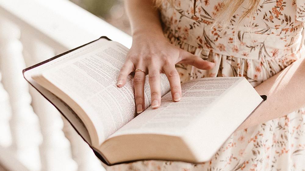 Eine Frau in einem geblümten Kleid liest in der Bibel.