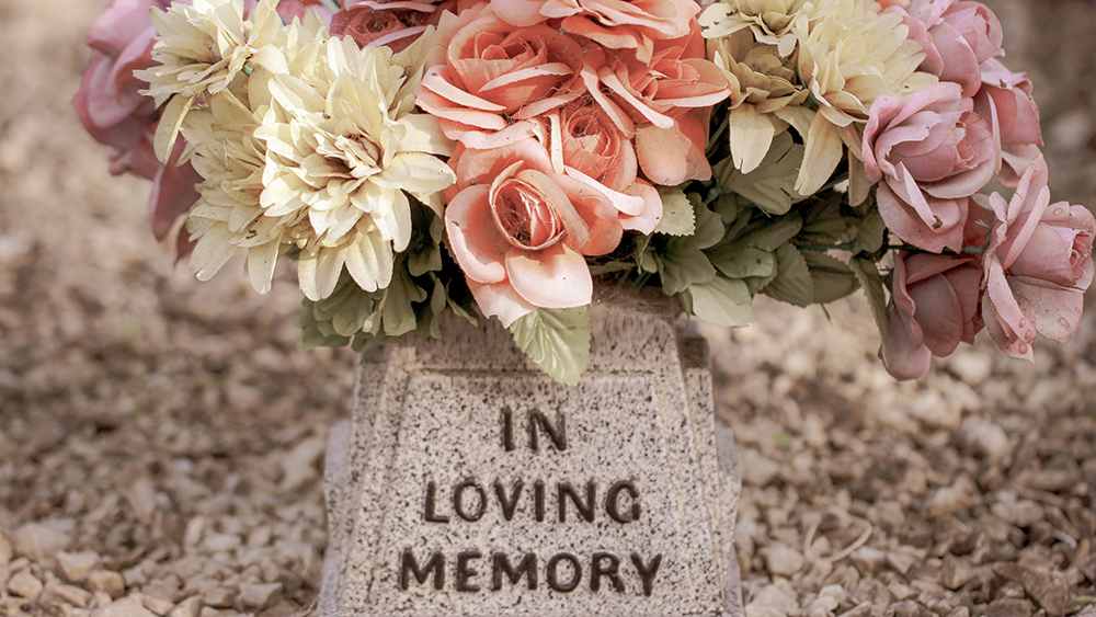 Ein Grabstein mit den Worten "In loving memory", darüber ein Blumenbouquet in beige-rosa.