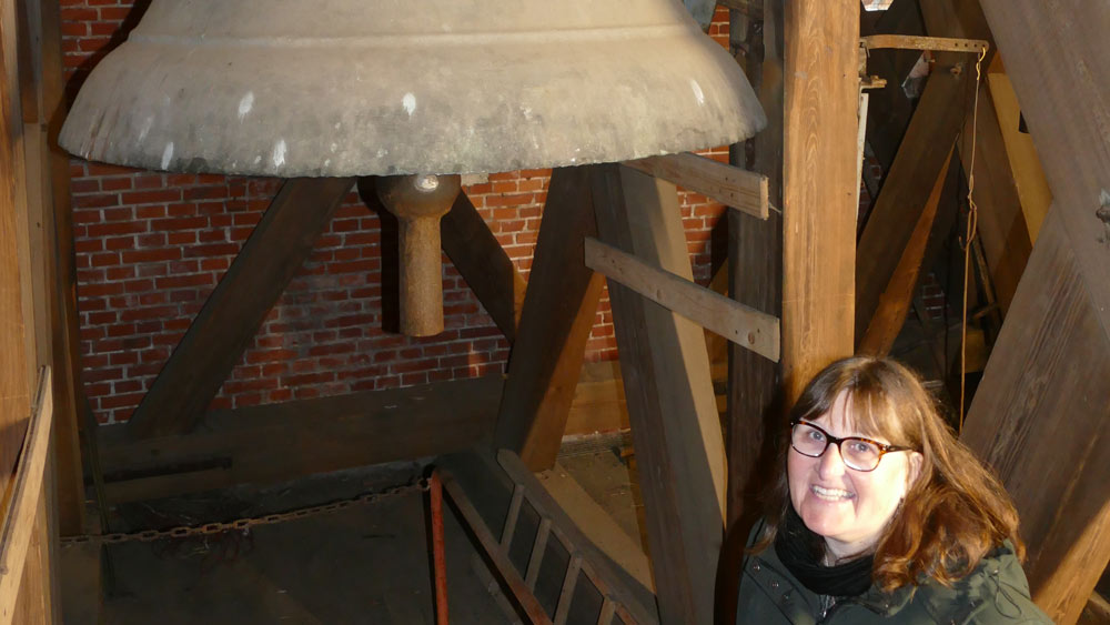 Frau steht im Glockenturm unter der Glocke, für die sie Spenden sammelt