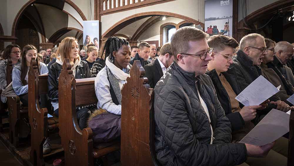 Viele Menschen sitzen auf Kirchenbanken und singen