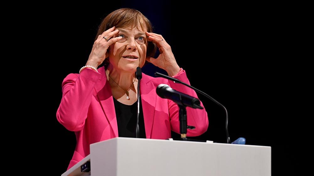 Frau im lila Blazer fasst sich an Rednerpult an den Kopf