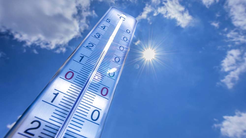 Thermometer vor blauem Himmel und heller Sonne