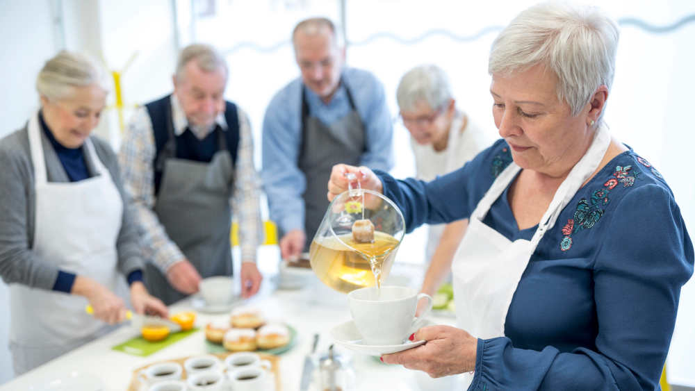 Ältere Frau gießt Tee in Tasse für Kaffeeparty im Altersheim