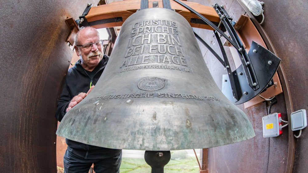 Kirchenältester Helmut Huber neben der untersten und grössten Bronzeglocke mit der Inschrift "Christus spricht: Ich bin bei euch alle Tage"