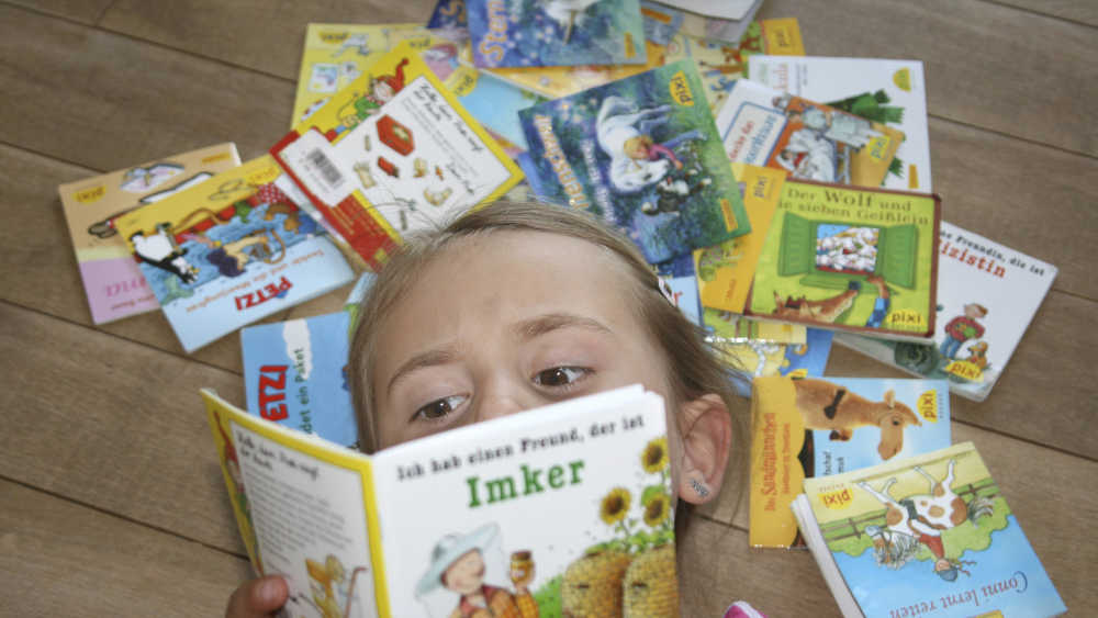 Ein Mädchen schmökert in ihren Pixi-Büchern