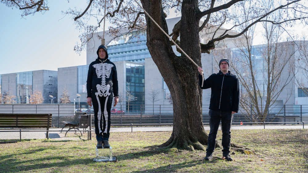 Klimaaktivist Wolfgang Metzeler-Kick steht mit einer Schlinge um den Hals auf einem schmelzenden Eisblock im Berliner Regierungsviertel