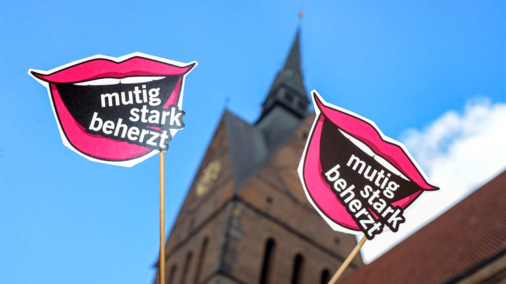 Das zentrale Motiv ist ein geöffneter Mund im Popart-Stil, in dem die Worte der Kirchentags-Losung stehen: "mutig - stark - beherzt"