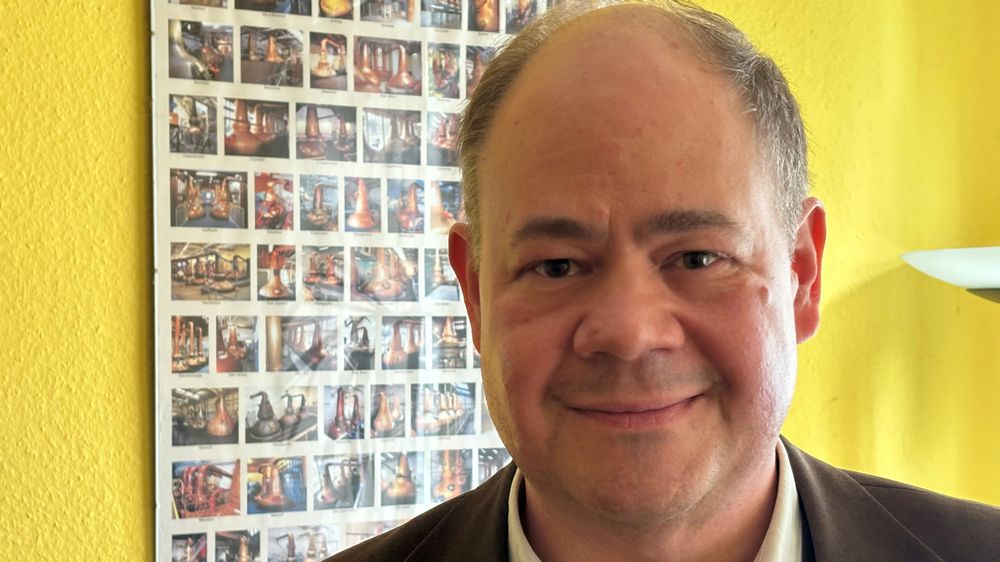 "In Single-Malt-Whiskys ist die Landschaft hineindestilliert, sagt Pastor Bernd Piorunek. Ein Poster hinter ihm zeigt verschiedene Destillerien in Schottland.