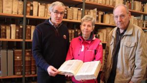 Bruno Blüggel von der Universitätsbibliothek Greifswald in der Bibliothek des Geistlichen Ministeriums zeigt zusammen mit Gisela Ros und Claus Wiggers ein mittelalterliches Handschriftenbuch.
