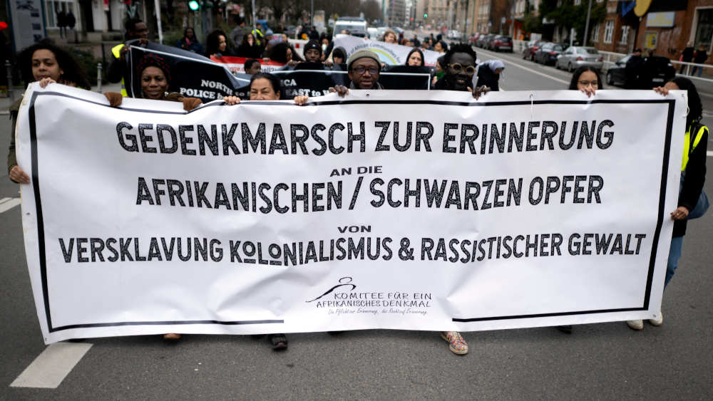 Der Verein „Decolonize Berlin“ setzt sich für Entschädigungen für deutsche Kolonialverbrechen in Afrika ein: Hier eine Demonstranten mit Transparent beim 17. Gedenkmarsch zur Erinnerung an die afrikanischen und schwarzen Opfer von Versklavung Kolonialismus und rassistischer Gewalt am 25.02.2024