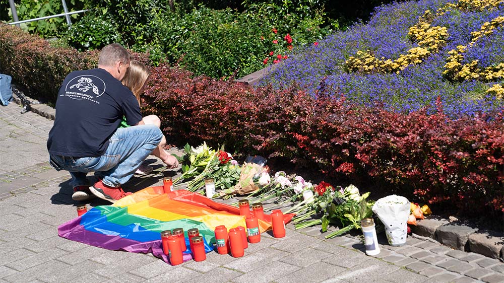 Nahe dem Tatort niedergelegte Blumen, Kerzen und eine Regenbogenflagge