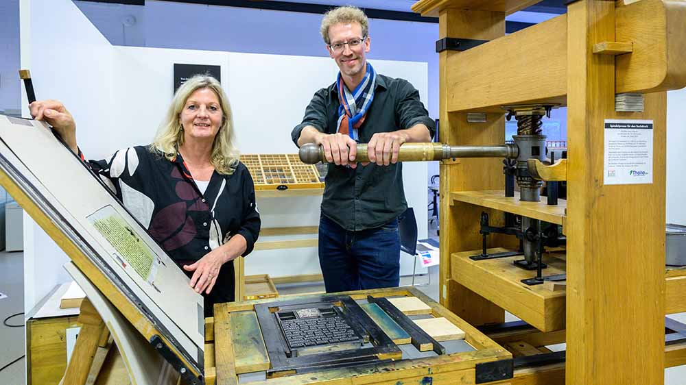Die Museumsleiterin Heike Düselder und der Kurator Ulfert Tschirner demonstrieren eine historische Druckmaschine.