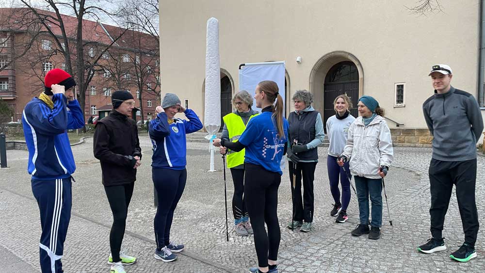 Friederike Feldmann verteilt Kärtchen mit Denkanstößen an die Teilnehmenden vor der Lindenkirche in Berlin-Wilmersdorf