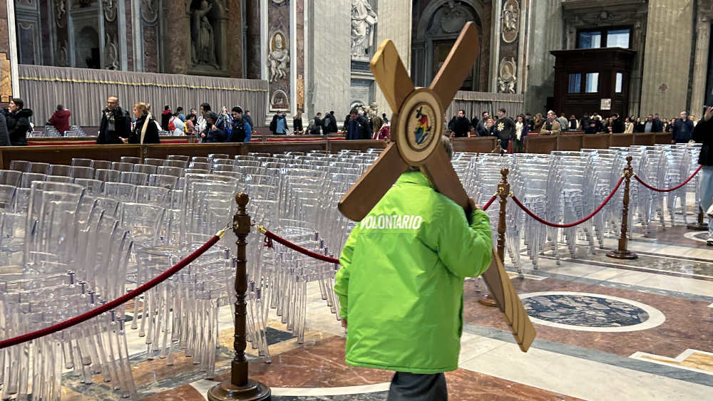 Ein Ehrenamtlicher in grüner Jacke nimmt das Holzkreuz und verschwindet damit zügigen Schrittes in Richtung Ausgang