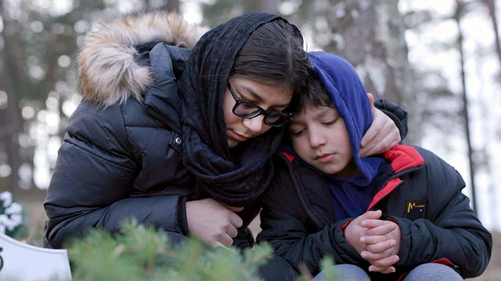 Runa und einer ihrer Brüder sitzen auf dem Friedhof vor dem Grab ihrer Mutter