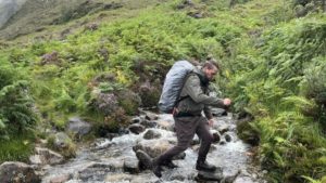 Ein Mann wandert durch einen kleinen Fluss in den Bergen