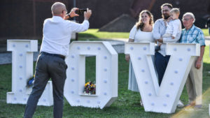 Hochzeitspaar steht hinter einem großen Schriftzug "LOV" und wird von einem Mann fotografiert