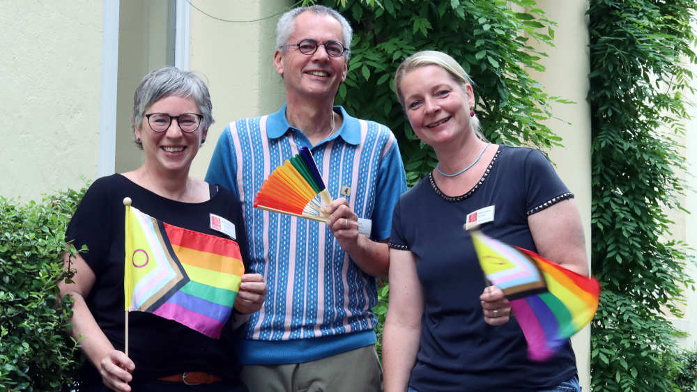 Übergriffe und Hasskommentare gegen Lesben, Schwule und Bisexuelle nehmen in Deutschland zu. Das Hospiz Leuchtfeuer in Hamburg-St. Pauli hält mit queerer Pflege dagegen. Hospizleiterin Melanie Fischer, Pflegedienstleiter Uwe Buehrle (Bührle) und Hauswirtschafterin Alexandra Schlath (v.li.) halten Regenbogen-Wimpel
