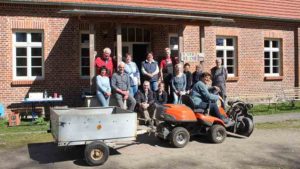 Menschen mit einem kleinen Traktor vor einem Haus in die Kamera schauend. Links ist ein Schild: Haus der Kirche