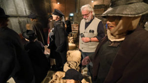 Älterer Mann mit mit Weste steht in einer Kulisse einer Hafenszene aus dem Jahr 1888