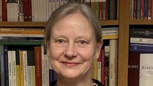 Frau mit kurzem Haar steht vor einem Bücherregal.