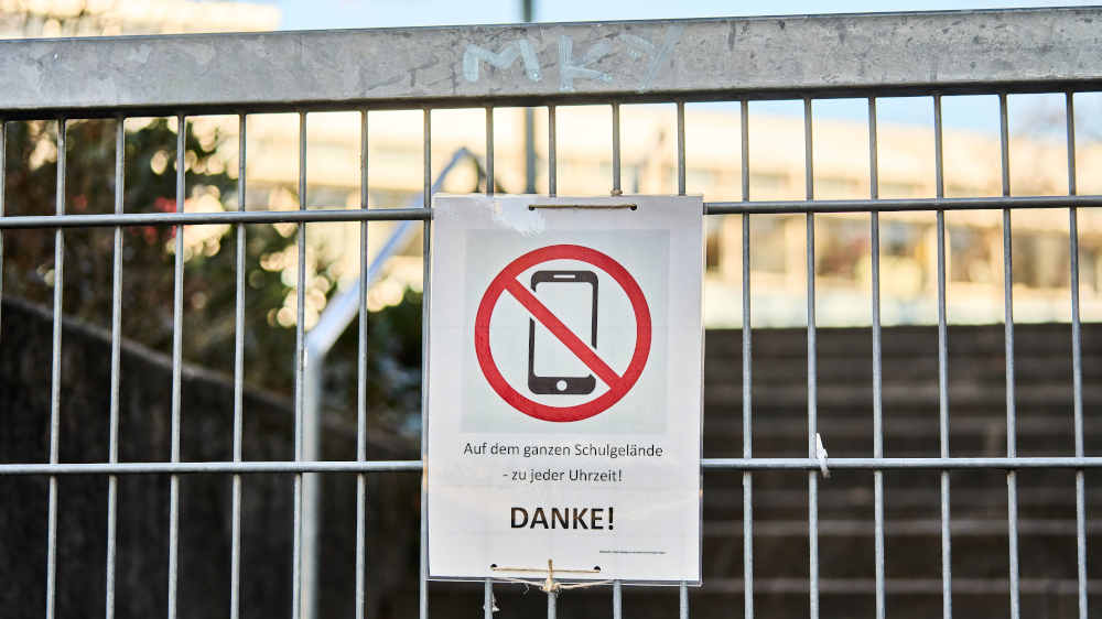 Ein Verbotsschild am Eingang eines Schulgeländes weist auf ein Verbot der Handynutzung hin (Archivbild)
