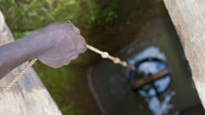 Kind, das mit Eimer und Seil Wasser aus einem Tiefbrunnen schöpft,