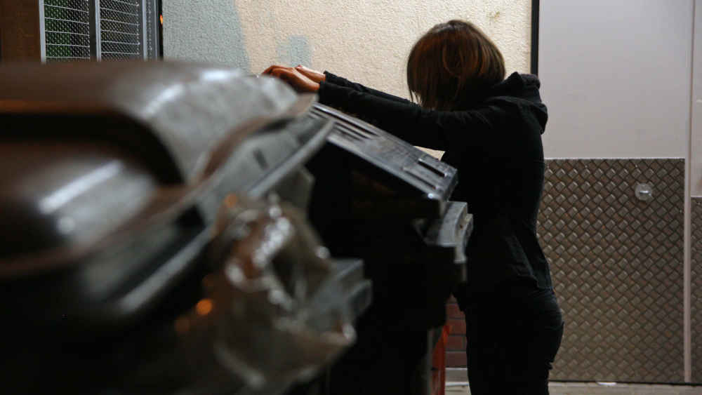 Containern: Jugendliche sucht bei Nacht nach Lebensmitteln in einer Mülltonne eines Supermarktes