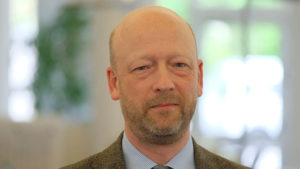 Ein Mann mittleren Alters mit Anzug sieht in die Kamera.